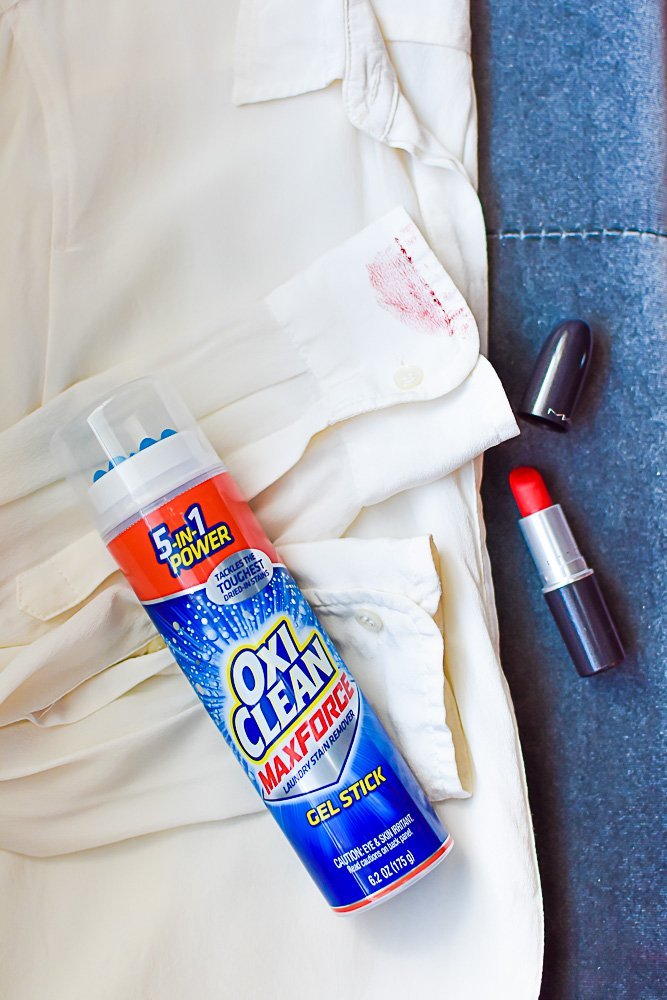 flat lay of stained white shirt, tube of red lipstick, and OxiClean gel stick