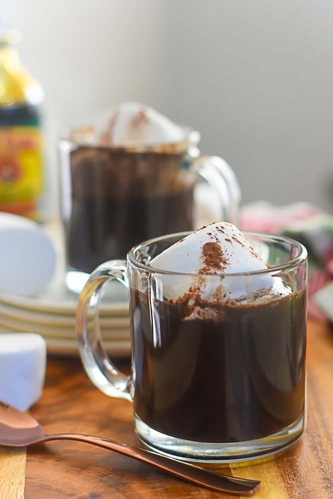 two mugs of bourbon gingerbread hot cocoa surrounded by jumbo marshmallows