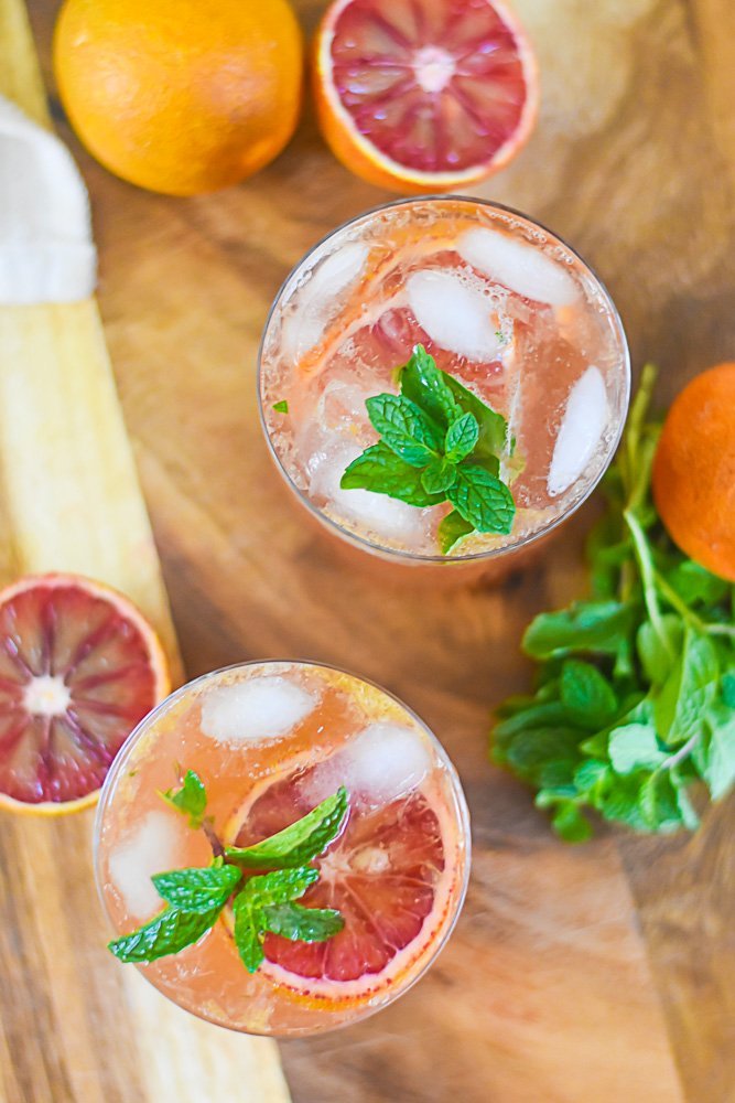 overhead view of two bourbon cocktails in rocks glasses with fresh mint and blood orange garnishes.