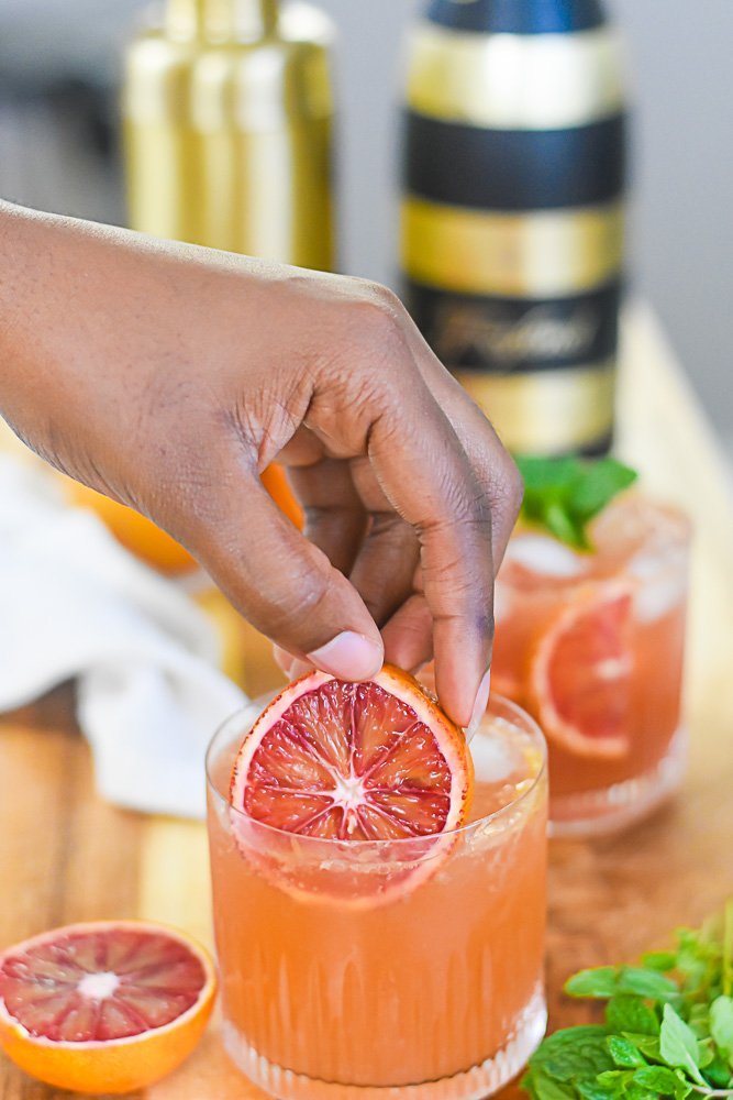 placing blood orange slice into rocks glass with bourbon cocktail