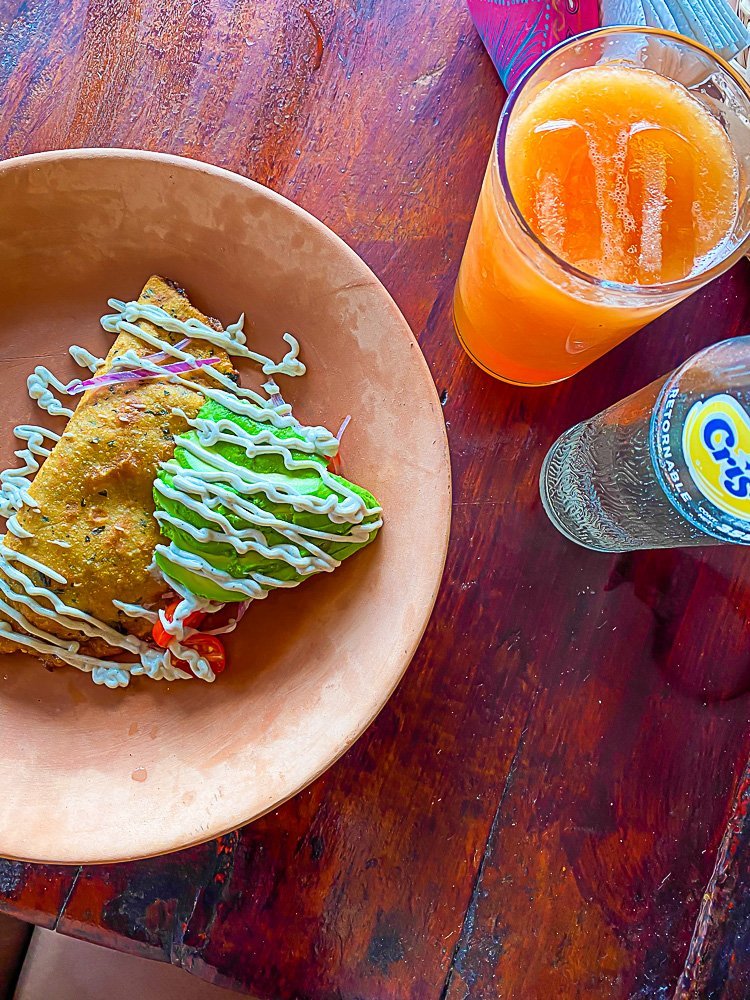 fried empanada and fresh avocado on terra cotta plate next to glass of fresh papaya juice