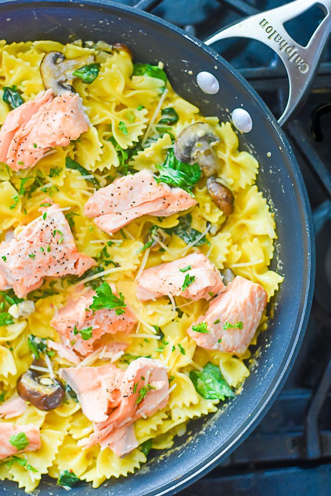 pan of cooked pasta, mushrooms, and spinach with pieces of cooked salmon on top