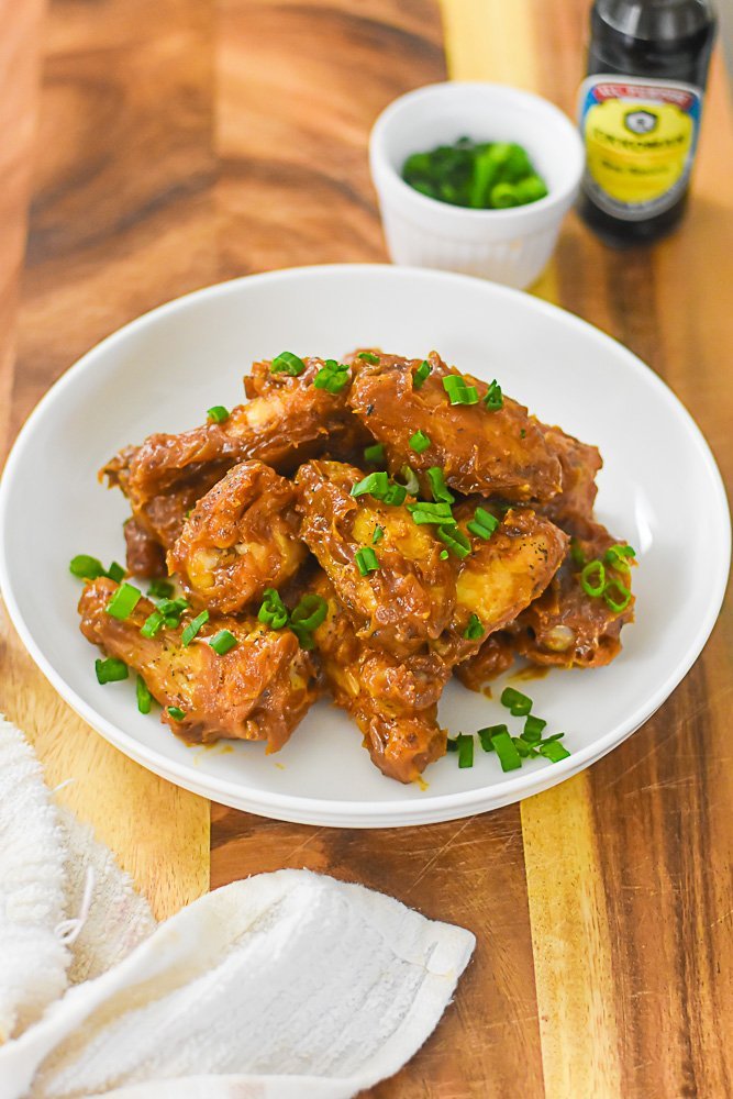 sauced peanut butter chicken wings in bowl, garnished with chopped green onion