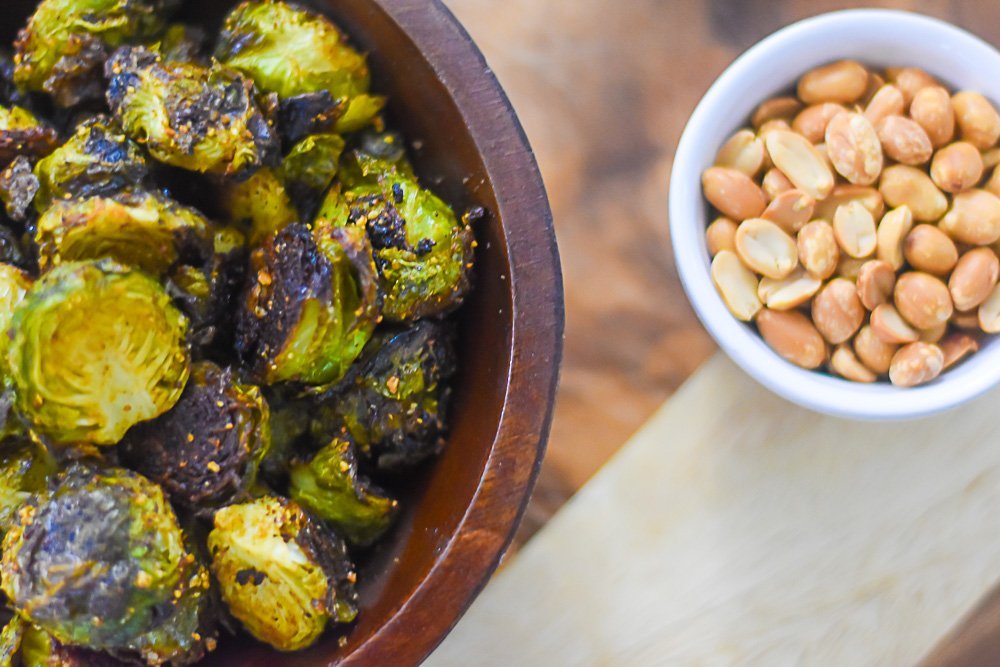 bowl of roasted brussles sprouts next to smalller bowl of groundnut (roasted peanuts).