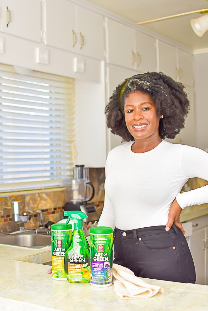 Jazzmine standing in kitchen with Art of Green natural cleaning products on counter.