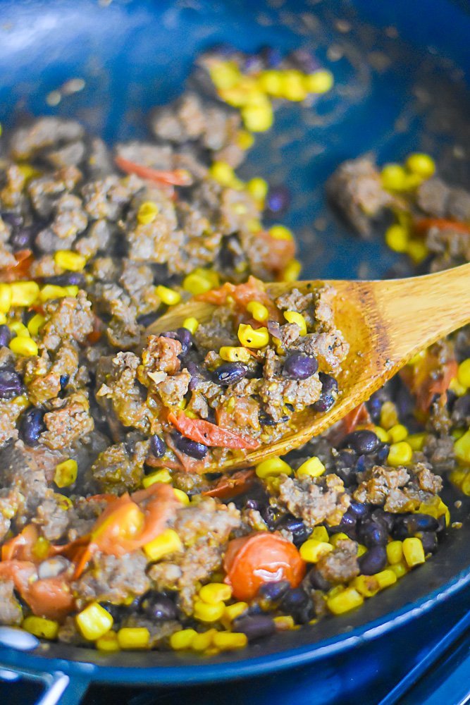 ground beef, baby tomatoes, black beans, and corn in skillet with wooden spoon.