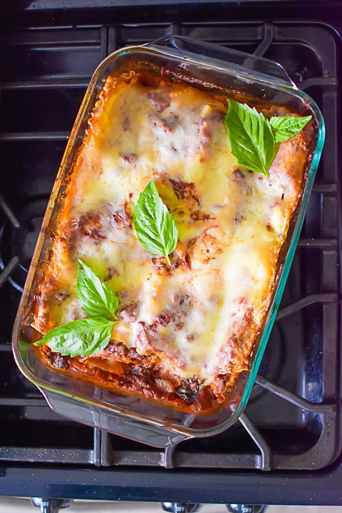 baked pan of lasagna with red wine sauce on stove top, garnished with fresh basil leaves.