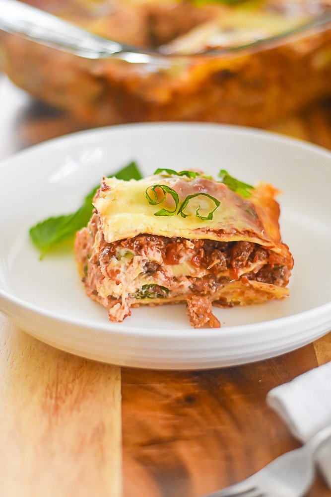 piece of three cheese lasagna on plate, garnished with fresh basil.