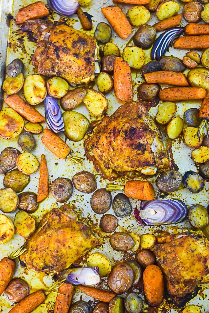 full sheet pan of Moroccan-spiced roasted chicken thighs, red onion, carrots, and baby potatoes.