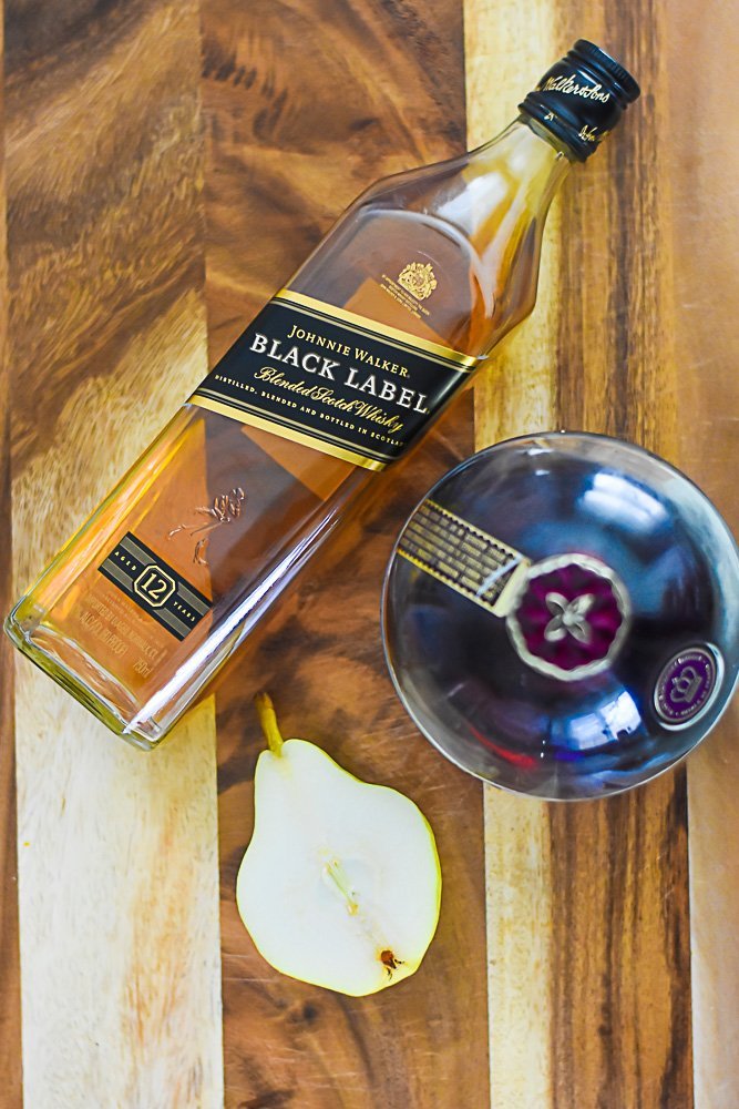 bottle of johnnie walker black label, chambord raspberry liqueur, and halved pear on cutting board.