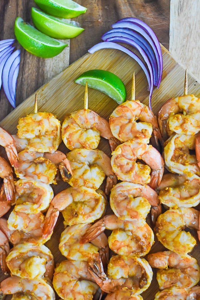 skewers of suya shrimp with slices of red onion and wedges of lime.