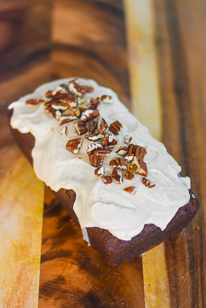 carrot cake loaf frosted with praline cream cheese frosting and garnished with chopped pecans.