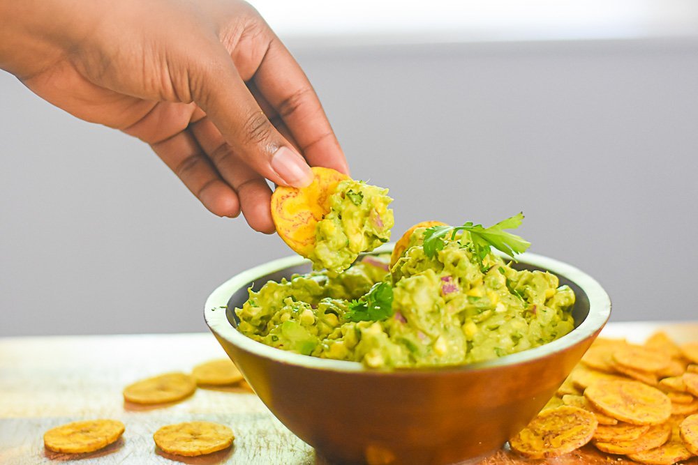 dipping plantain chip into bowl of grilled sweet corn guacamole.