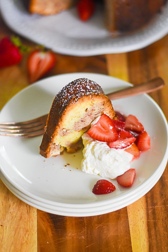 slice of strawberry sour cream pound cake on plate with whipped cream and strawberries.
