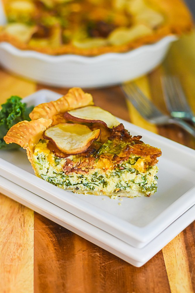 slice of bacon kale quiche with crispy red potato slices on top on white plate.