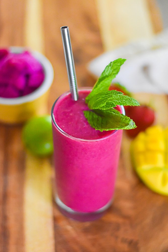 pink pitaya smoothie in tall glass with metal straw and fresh mint leaf garnish.