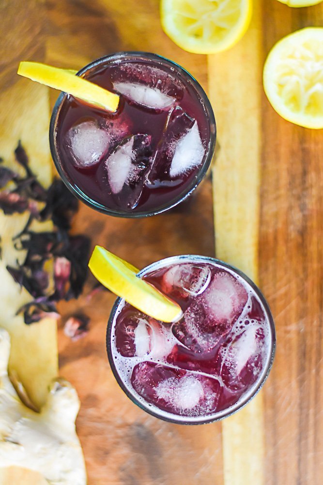 two glasses of zobo lemonade with lemon slice garnishes on a wooden countertop.