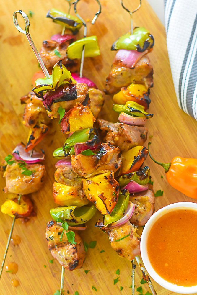 cooked pork and vegetable skewers garnished with chopped parsley on wood cutting board.