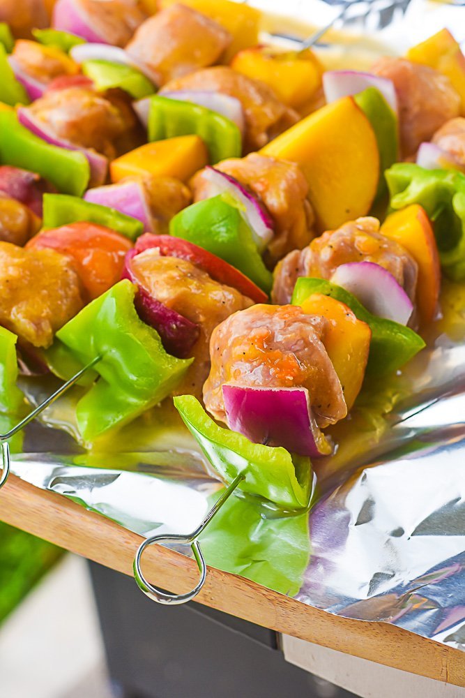 prepped skewers with green bell pepper, red onion, marinated pork tenderloin, and peach ready for grilling.