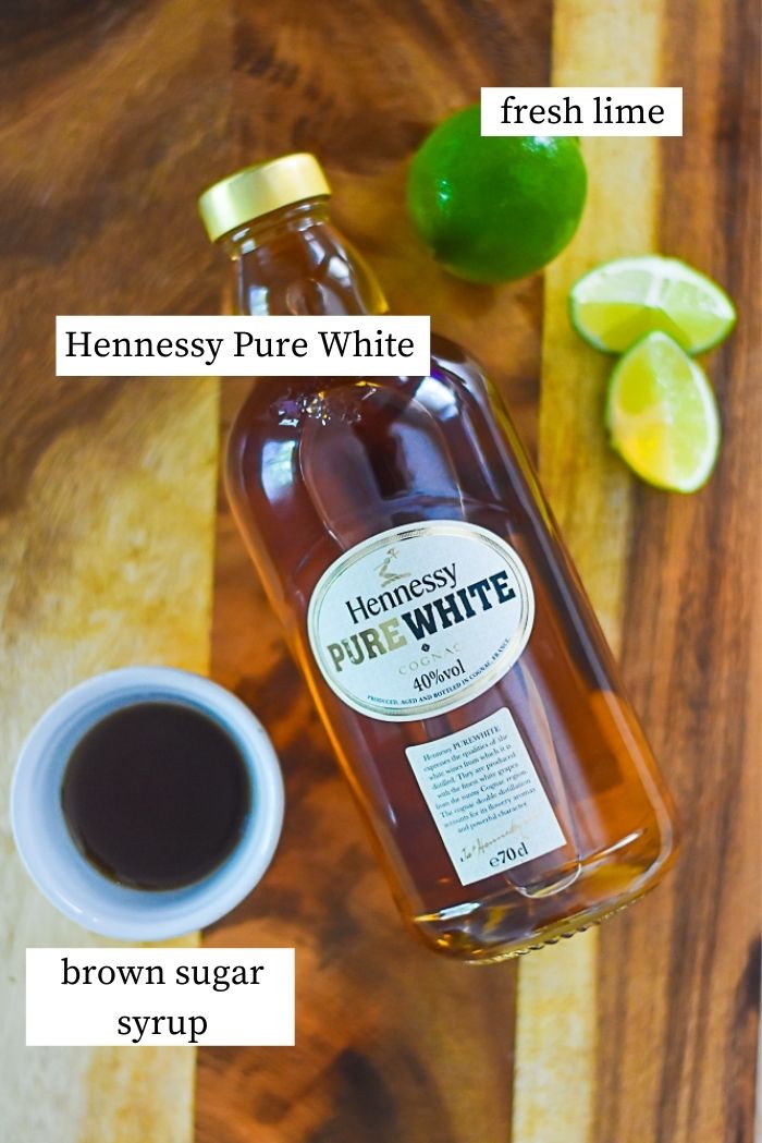 flat lay of bottle of hennessy pure white, brown sugar simple syrup, and fresh lime on cutting board.