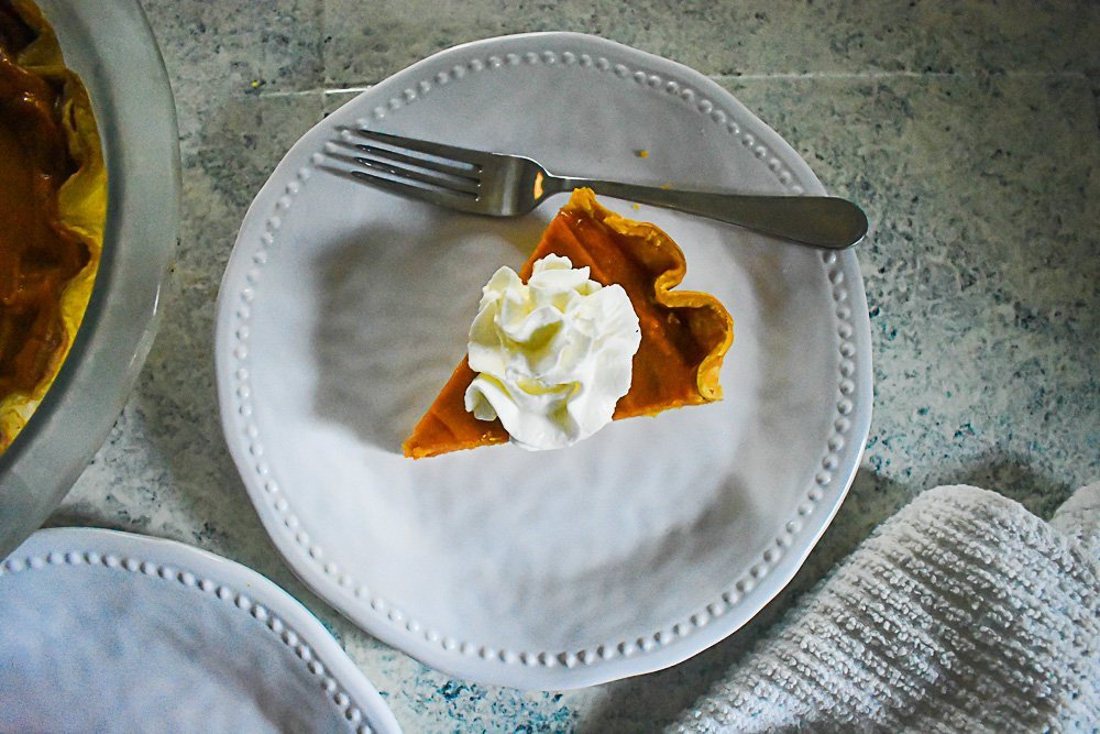 slice of sweet potato pie on white plate with whipped cream on top.