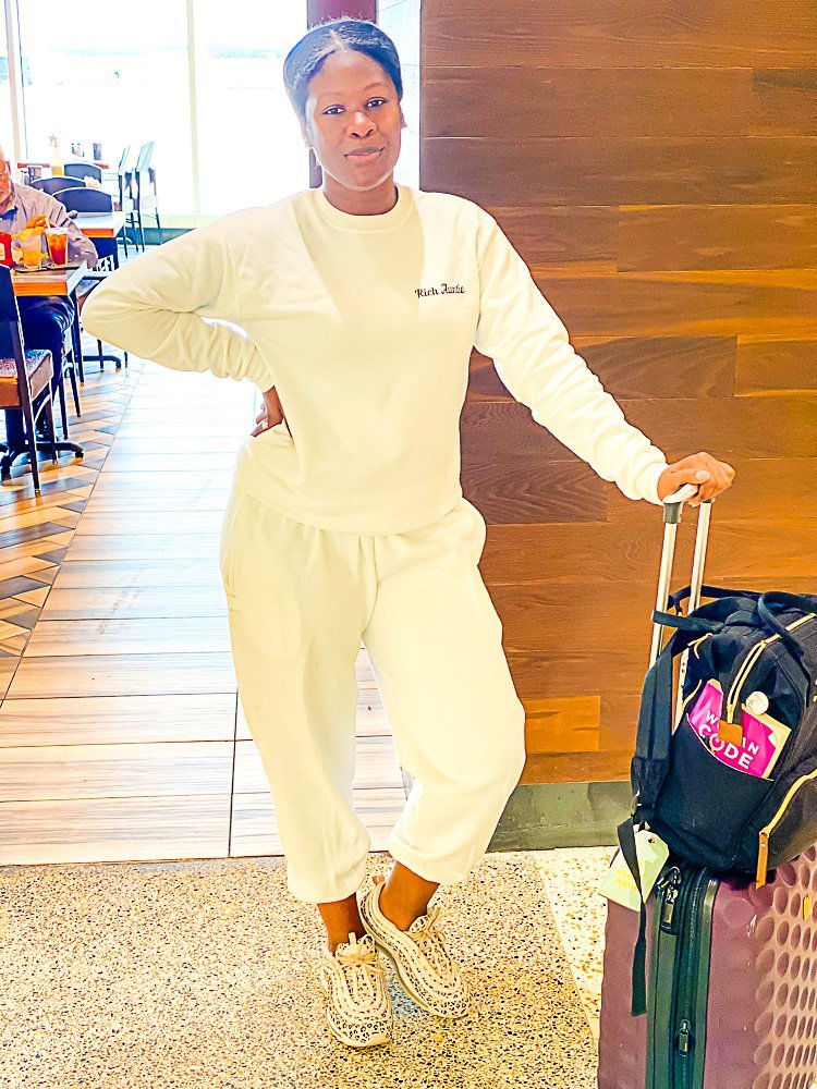 Jazzmine standing in airport wearing all white sweat suit and leopard sneakers.