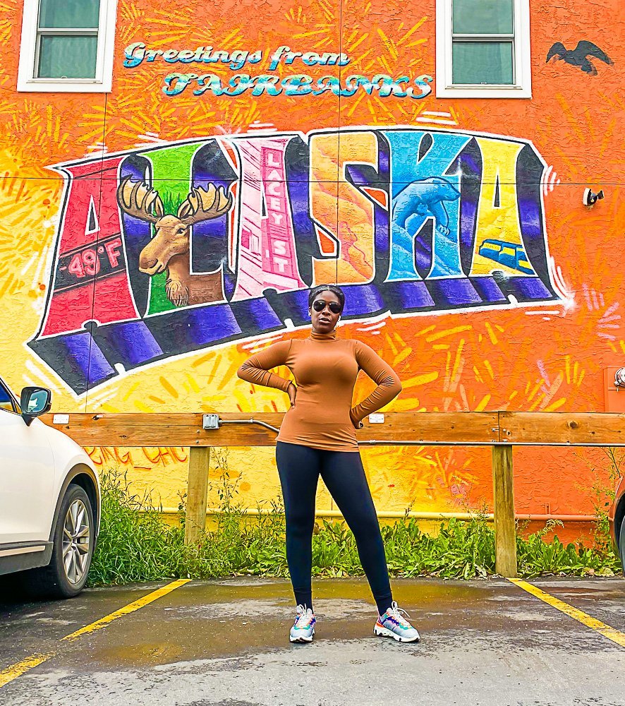 Jazzmine standing in front of "Greetings from Fairbanks, Alaska" mural.
