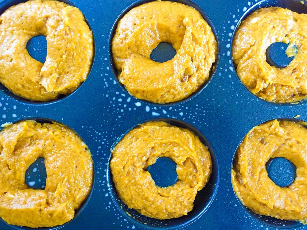 pumpkin cake batter piped into a donut pan.