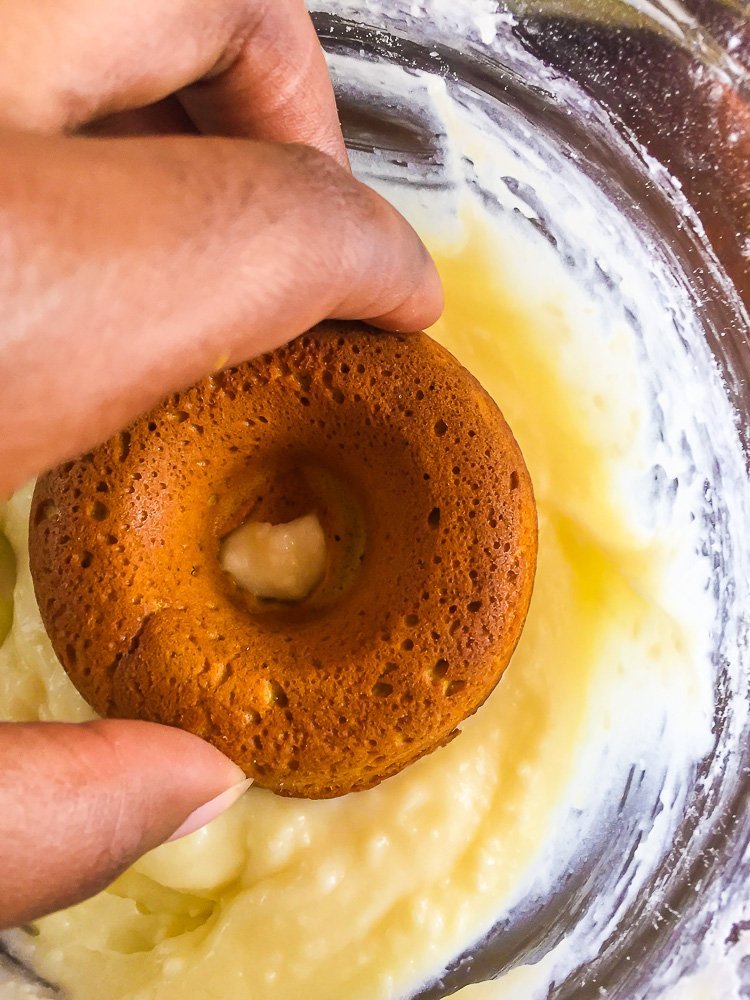 placing pumpkin donut into bowl of cream cheese frosting.
