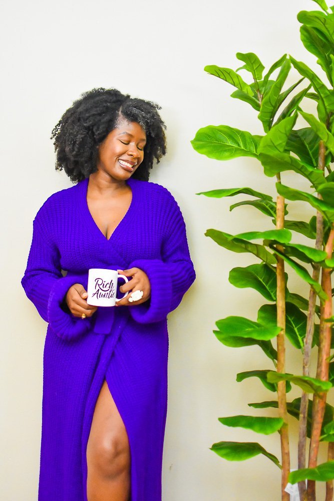 Jazzmine holding glossy mug wearing floor-length purple cardigan dress.