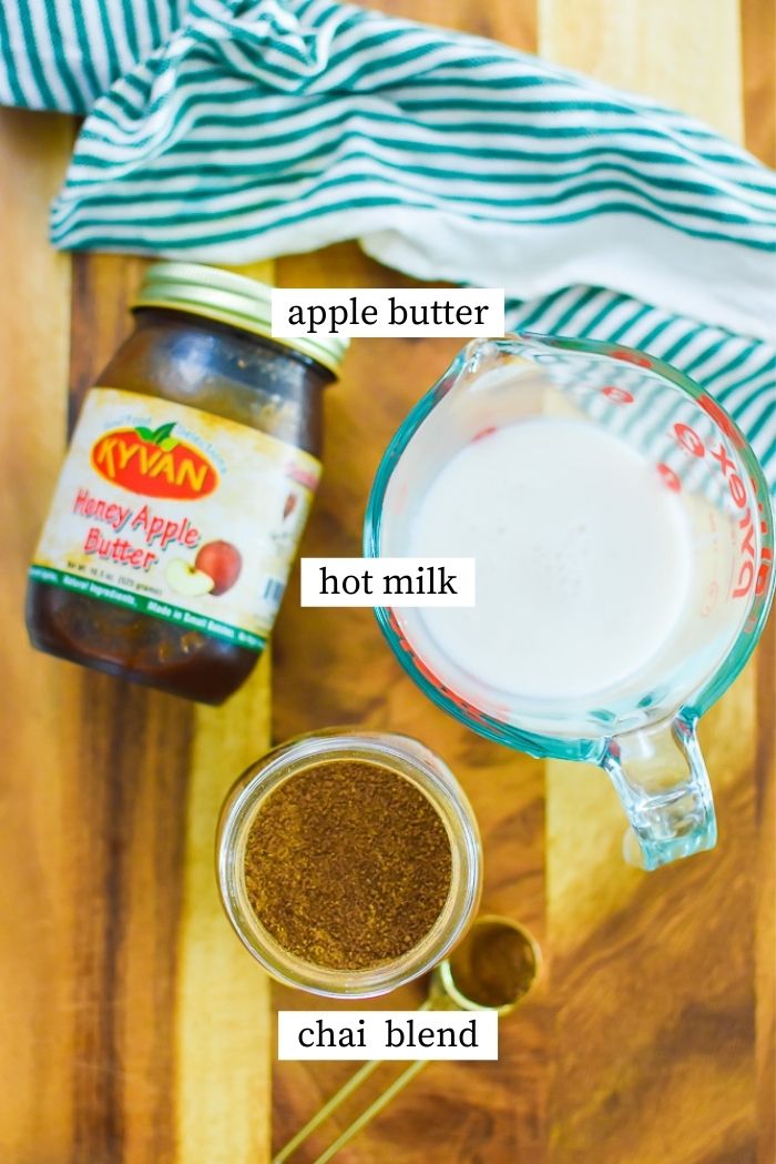 jar of apple butter, jar of chai spice blend, and small pitcher of milk on wooden cutting board.