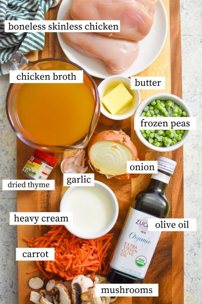 creamy chicken mushroom soup ingredients on cutting board: mushrooms, carrots, olive oil, butter, onion, garlic, cream, thyme, chicken broth, chicken breast, and peas.