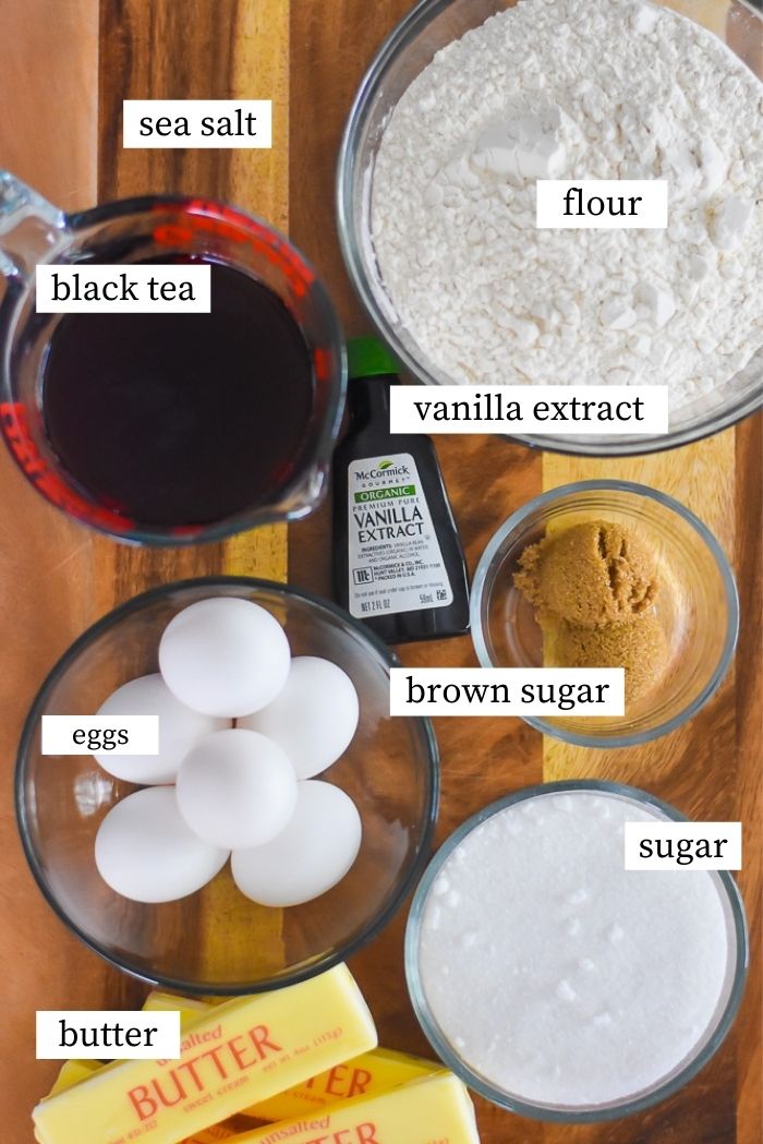 sweet tea pound cake ingredients on wooden cutting board: butter, eggs, sugar, brown sugar, vanilla extract, flour, sea salt, and black tea.