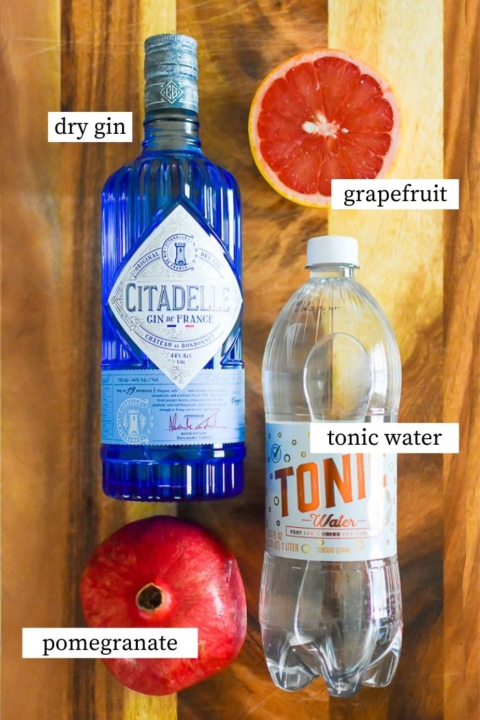 flat lay of bottles of gin and tonic water, pomegranate, and grapefruit on wooden cutting board.