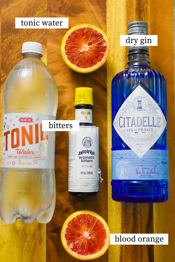 tonic water, angostura bitters, gin, and blood orange on cutting board.
