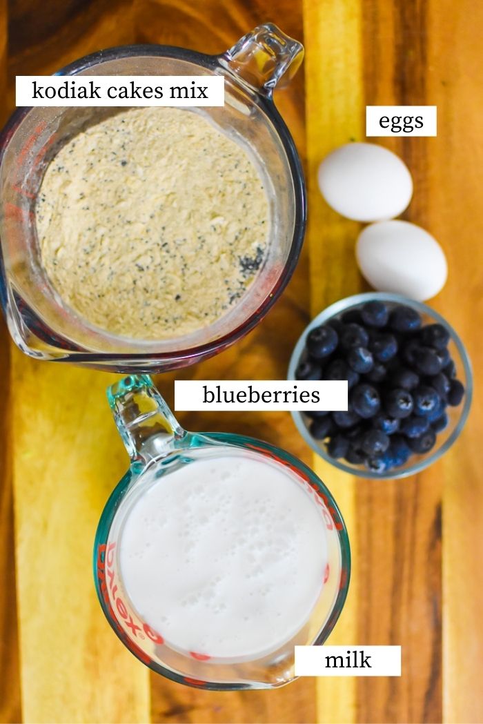 milk, blueberries, pancake mix, and eggs on wooden cutting board.