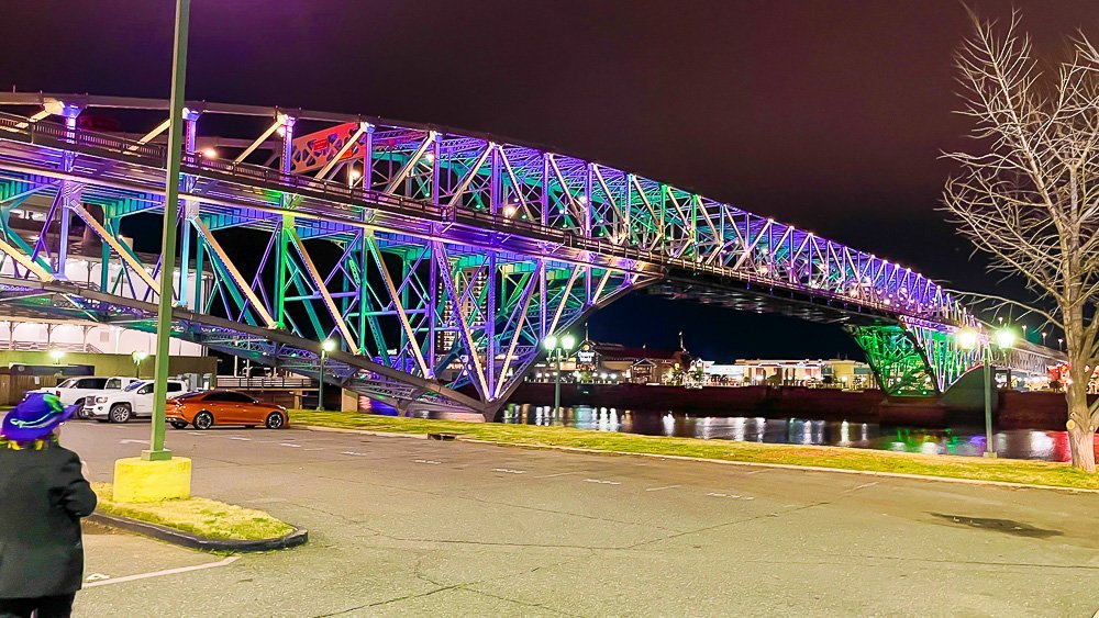 Long-Allen bridge lit up in Mardi Gras colors at night.