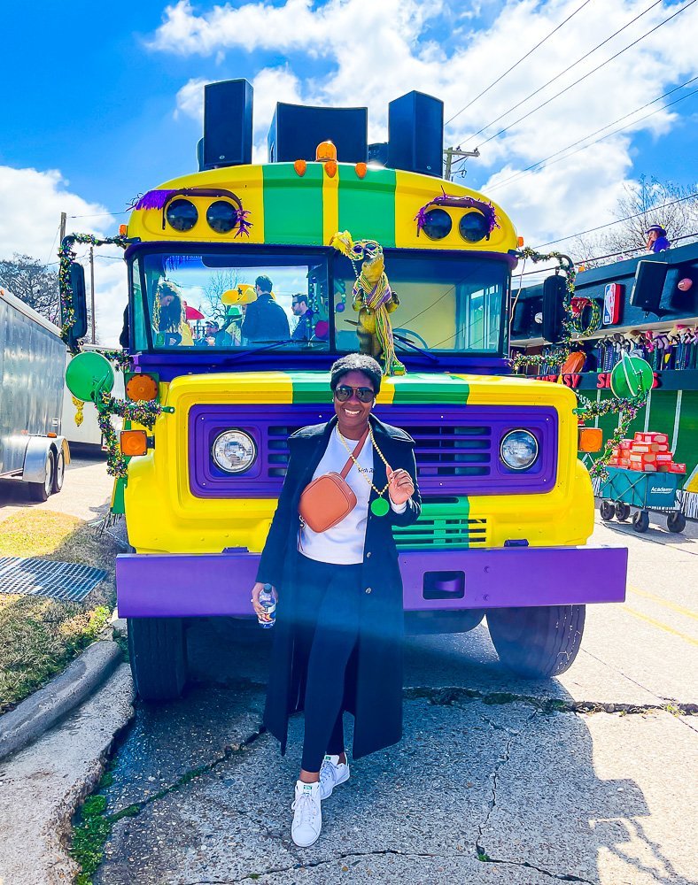 Jazzmine standing in front of purple, green, and yellow painted bus at Shreveport Mardi Gras parade.