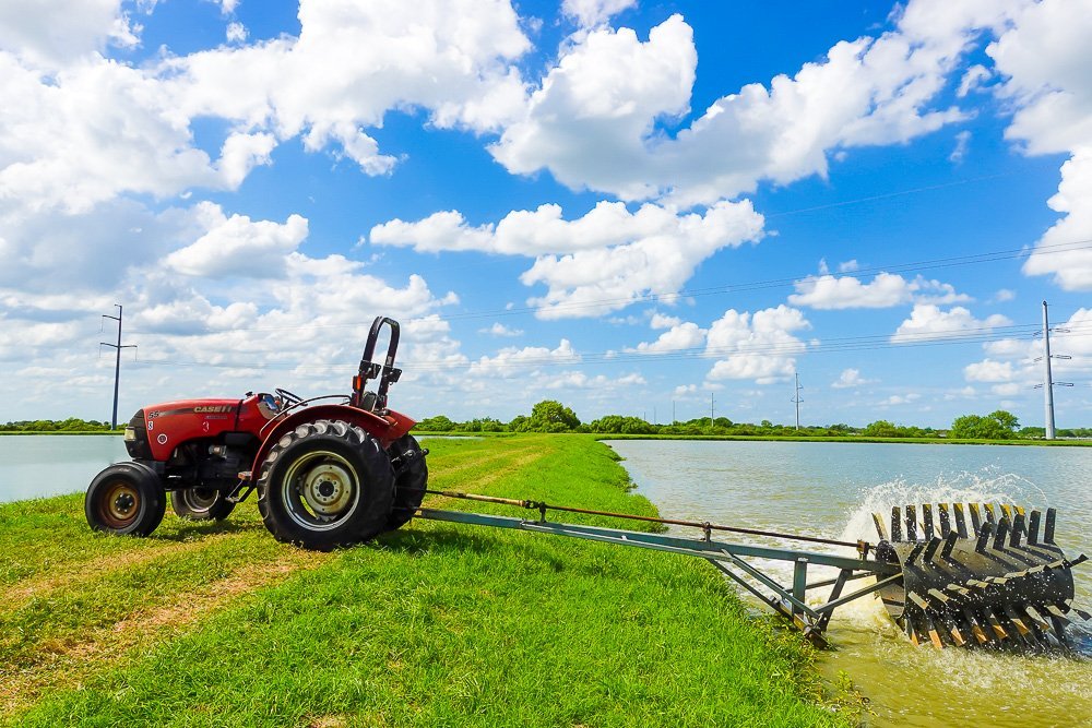 tractor next to pond of water on catfish farm.
