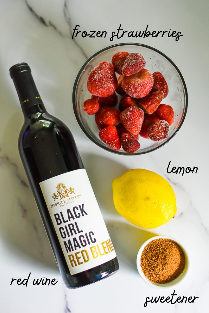 bottle of red wine, coconut sugar, lemon, and bowl of frozen strawberries on white granite countertop.