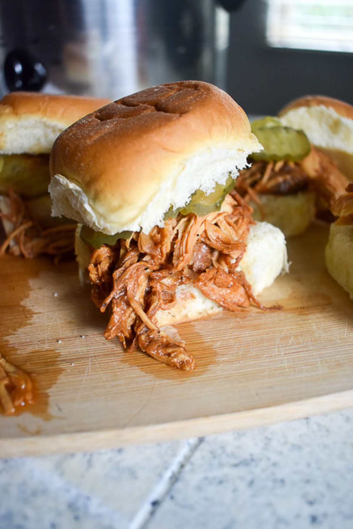 slow cooked bbq chicken sliders made in a crockpot and served on a King's Hawaiian roll with pickles.