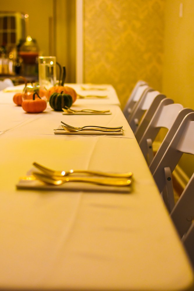 place setting with white napkins and gold disposable cutlery on long table.