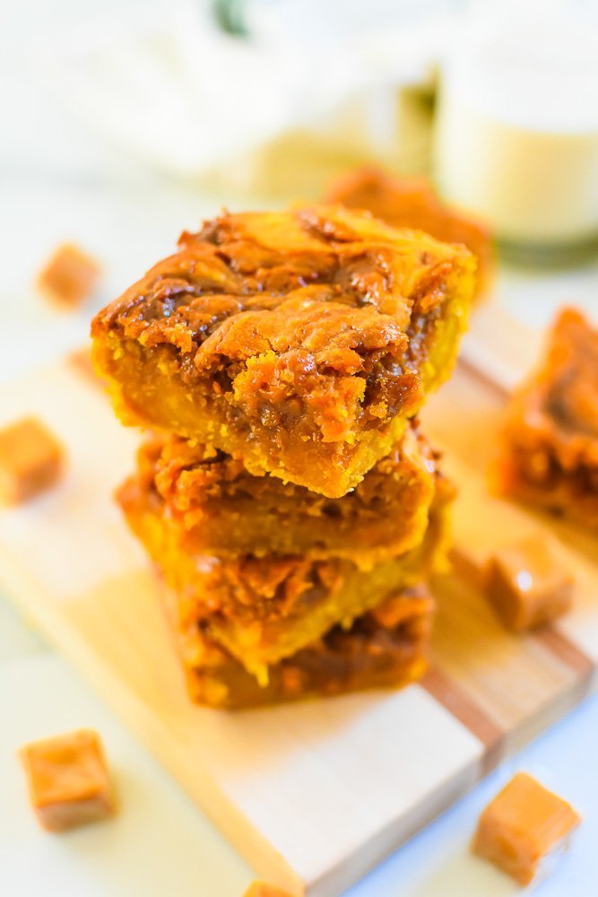 sweet potato and salted caramel dessert bars stacked and surrounded by wrapped caramel candies.