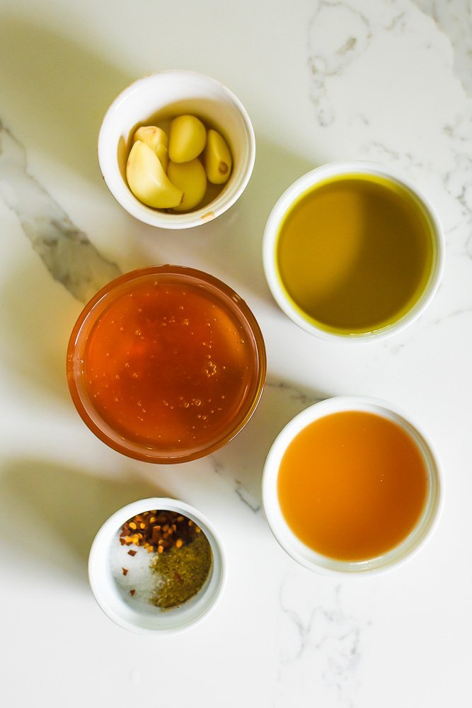 ramekins of spices, honey, garlic, olive oil, and apple cider vinegar on white granite counter top.
