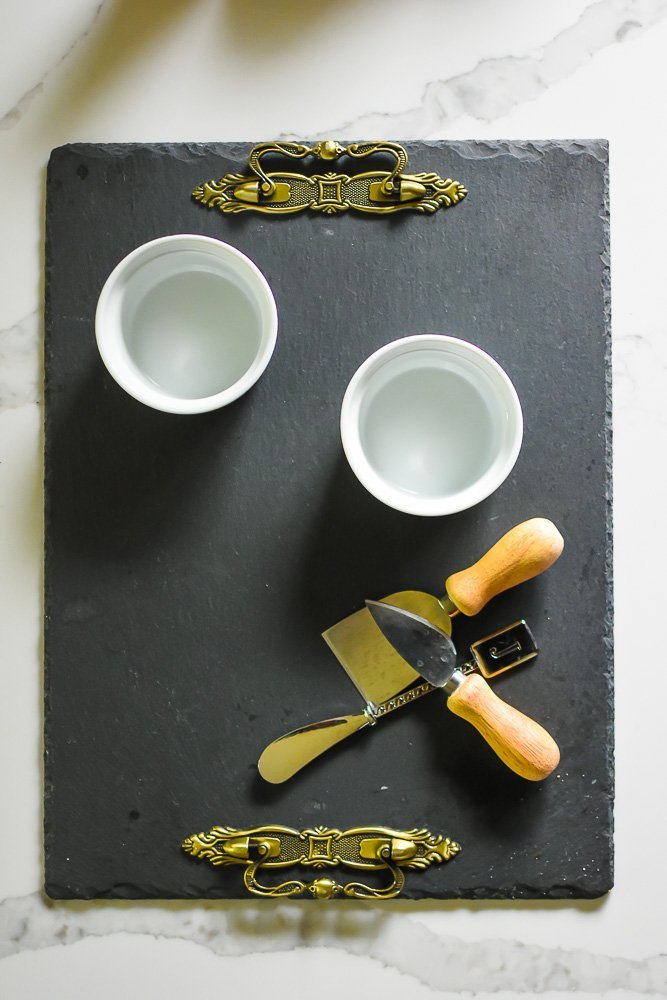 slate cheese tray, white ramekins, and cheese knives on white counter top.
