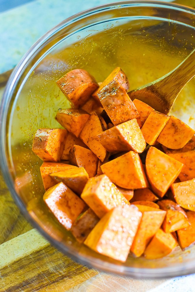 sweet potato chunks tossed in oil and spices in a large glass bowl.
