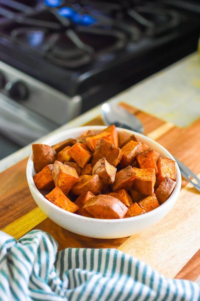 ceramic bowl of roasted sweet potato bites on wooden cutting board.
