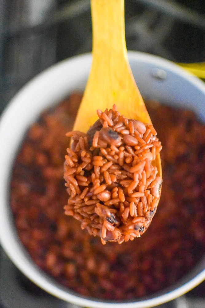 cooked Ghanaian rice and beans on wooden spoon.