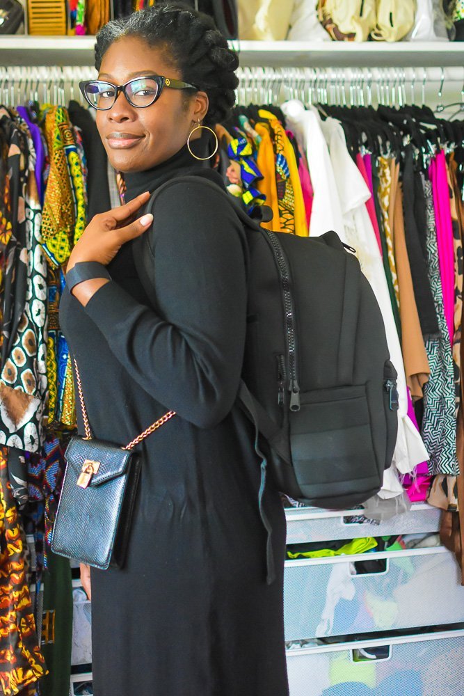 Jazzmine wearing a black sweater dress, small crossbody bag, and fully packed travel backpack.