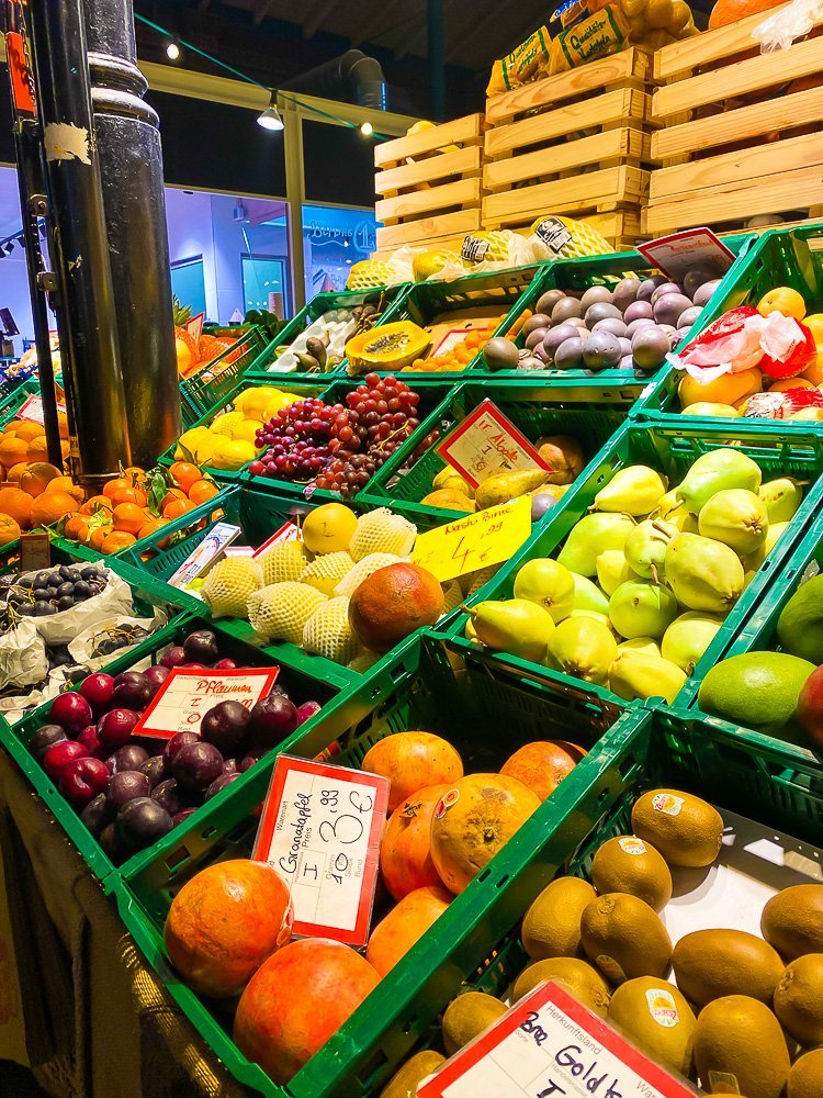 assorted fresh fruit in green crates inside a Berlin food hall at night.